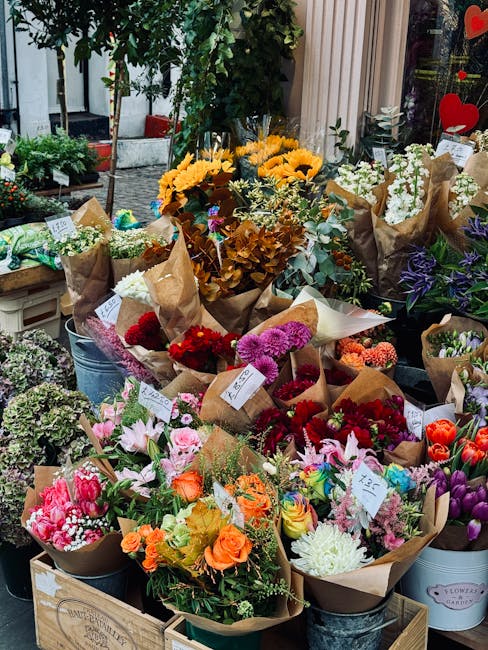 A vibrant display of freshly cut flower bouquets arranged on a market stall, featuring a variety of blooms including bright yellow sunflowers, pink lilies, orange roses, red and purple carnations, whi